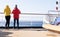 Two cruise passengers stand at the railing at the stern of a cruise ship and look back at the open sea