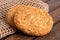 Two crunchy oat and wholemeal biscuits lying on brown burlap on dark wood