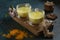 Two cups of ayurvedic drink golden milk turmeric latte with curcuma powder, ginger and honey over green texture background