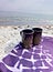 Two cups on a blanket on the beach.