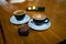 two cups of cappuccino on black cups, on wooden table, with typical brasilian sweet called brigadeiro. Cell phone on the backgroun