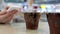 Two cups of coca cola on table with woman reading message on iphone at food court