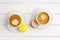 Two cups of coffee cappuccino and two macaroons lemon and chocolate on white wooden table.