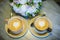 Two cups of coffee stand on the table against bouquet of flowers