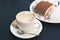 Two cups of coffee and tiramisu on black table background with beautiful latte art heart shaped.