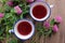 Two cups of healing herbal tea or infusion with red clover, purple flowers on the wooden table. Natural floral background.