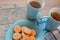 Two cups of tea on a blue napkin. Biscuits on a blue plate on a wooden background