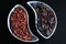 Two curved bowls with dried goji berries and grapes opposite each other on a black background