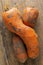 Two curved ugly carrots with pieces of soil on brown old wooden background. Vegetables with unusual strange shape