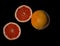 Two cut halves bright red orange grapefruit and whole fruit on black backdrop