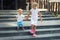 Two cute adorable caucasian blond little siblings walking down stiars residential building. Reliable elder sister