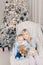 Two cute adorable little siblings brother and sister sitting in chair near christmas tree in cozy living room looking , dreaming