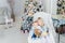 Two cute adorable little siblings brother and sister sitting in chair near christmas tree in cozy living room looking , dreaming