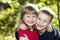 Two cute blond funny happy smiling children siblings, young boy brother embracing sister girl outdoors on bright sunny green bokeh