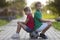 Two cute blond happy young children, smiling boy and long-haired girl sitting back-to-back on soccer ball on empty sunny suburb