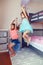 Two cute Caucasian girls siblings jumping from bed in room. Happy excited friends having fun at home. Adorable children playing