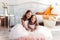 Two cute girls cuddle in a light room. Smiling children sitting together in bedroom looking in camera. Sibling love