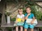 Two cute inquisitive preschoolers are sitting on table in yard, holding stacks of children`s books