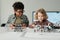 Two cute intercultural schoolboys playing with handmade toy robots by table