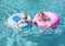 Two cute kids playing on inflatable tubes in a swimming pool on a sunny day