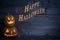 Two Cute Lighted Pumpkins with Happy Halloween Written on a Dark Blue Rustic Wood Board Background