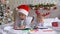 Two cute little girls sisters wearing Santa Helper hats write letter to Santa lying on bed at home in Christmas