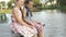 Two cute little girls are sitting on the river Bank on a wooden bridge at sunset on a summer evening. Portrait. Close up