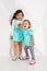 Two cute little girls standing in turquoise wear on the white wall background in the studio.