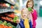 Two cute little sisters choosing broccoli in a food store or a supermarket