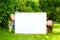 Two cute little sisters holding big blank whiteboard on sunny summer day outdoors