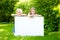 Two cute little sisters holding big blank whiteboard on sunny summer day outdoors