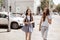 Two cute thin girls with long hair,wearing casual outfit, are walking down the street on a sunny day.