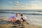 Two cute young sisters having fun on a sandy beach on warm and sunny summer day by the sea. Kids playing by the ocean