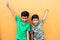 Two dark-haired latin male children standing in front of a yellow wall live in poverty without toys, dream, play, imagine a happy