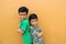 Two dark-haired latin male children standing in front of a yellow wall live in poverty without toys, dream, play, imagine a happy