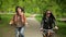 Two Dark-haired Women are Riding through the City Park. Beautiful Brunettes with Bicycles Enjoying Warm Sunny Weather