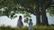 Two daughters walking along green field to their mother, swinging on a rope swing tied to old tree.