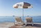 Two deckchairs under a parasol against the backdrop of a calm sea on a clear sunny day. Idyll and relaxation. Travel and tourism.