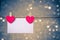 Two decorative red hearts with greeting card hanging on blue and golden light bokeh background, concept of valentine day