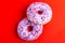Two delicious lilac donuts with sprinkle on bright red background