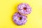 Two delicious lilac donuts with sprinkle on bright yellow background