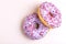 Two delicious lilac donuts with sprinkle on light marble background