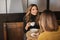 Two delighted women girlfriends drinking coffee and talking during meeting in cozy cafe