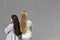 two different ethnic girls with long hair are standing back to each other, grey background wall, rear view