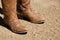 Two dirty western cowboy boots standing on dirt ground