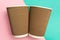 Two disposable cups for hot drinks on a geometric pink and turquoise backgrounds. Paper cups