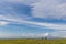 Two distant people walking on a green meadow in spring, below a big, deep sky