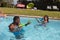 Two diverse male and female friends having fun playing with water guns in swimming pool