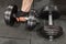 Two dumbbells on gym floor, one held by mans hand