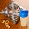 Two dumbbells, meter tape and plastic protein shaker on wood